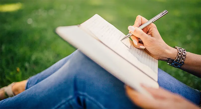 A lady scribbling in a notebook while sitting on grass