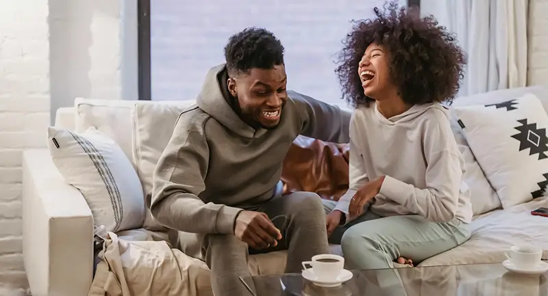 A black couple laughing on a sofa