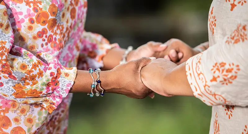 Two women in floral print dresses, holding hands.